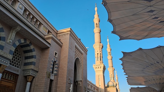 A front view of Al-Masjid An-Nabawi with its front gate, its minarets, and its giant umbrellas in the morning.