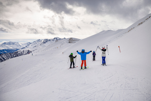 Mother and three teenage kids are skiing together in mountains on a cloudy winter day. 
Shot with Canon R5