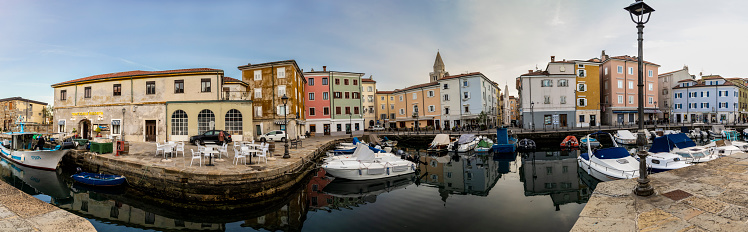 Muggia, Italy – November 18, 2023. Panoramic shot of the old harbour of Muggia, a coastal town in northern Italy near Trieste with moored small motor boats.