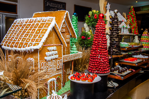 Gingerbread houses with cream frosting and sugar icing displayed for festive catering buffet among other variety of different sweets and desserts.