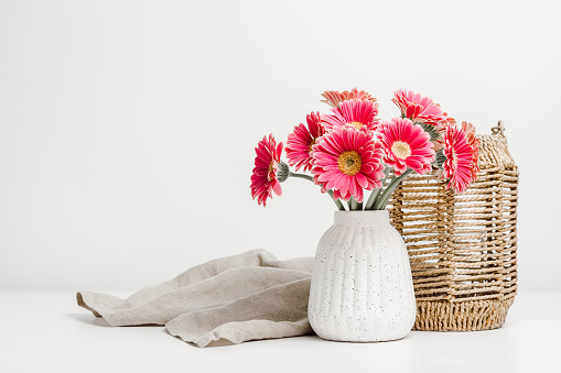 Vase with pink gerbera flowers and wicker lantern for candles at the background, scandinavian interior style