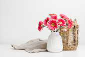 Vase with pink gerbera flowers and wicker lantern for candles at the background
