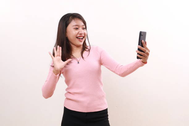 istock Cheerful young asian girl standing while doing video call on her phone. Isolated on white background 1807861020