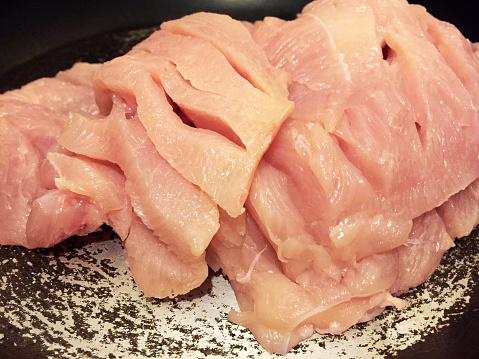 Raw chicken breast fillets in a frying pan for cooking