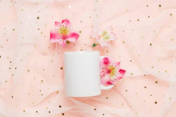 Photo of Mockup white mug with pink lily flowers on fabric with glitter