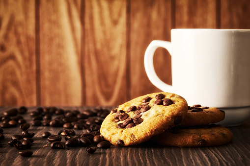 Dark image with white coffee cup, chocolate oat cookies and coffee grain. Breakfast backgrounds theme
