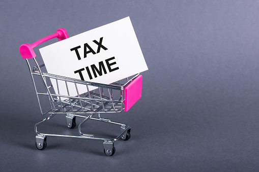 TAX TIME text on white sticky in a shopping trolley, gray background