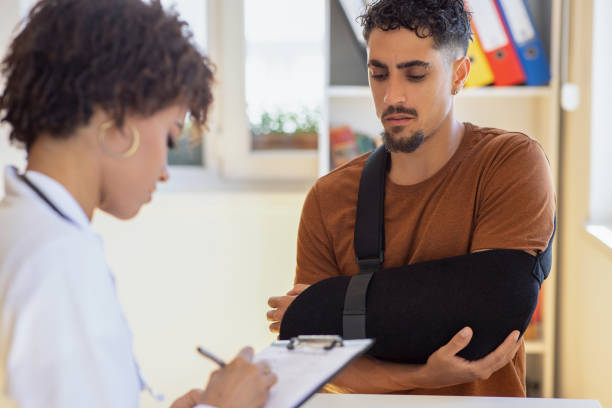 Doctor at hospital prescribing treatment and talking to young patient Doctor at hospital prescribing treatment and talking to young patient man with arm sling stock pictures, royalty-free photos & images