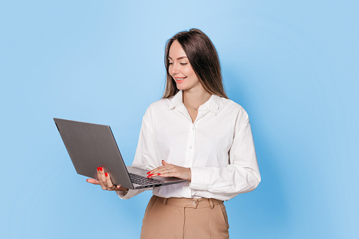 business woman with a laptop isolated on a blue background. young woman marketer working with laptop while standing