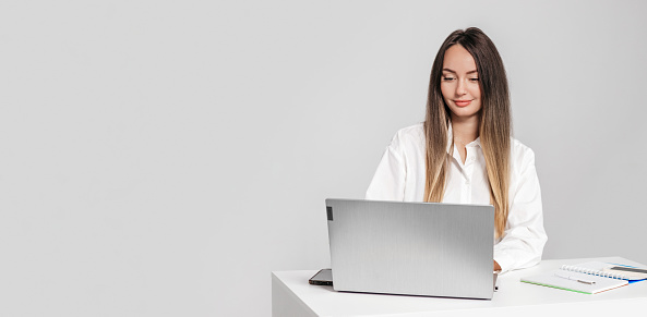 student girl psychologist sitting at a table with a laptop smiling at the camera isolated on a white background in the studio. copy space. web banner