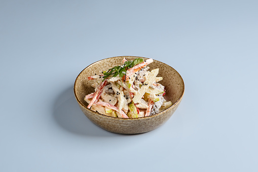 A delectable Eastern-style salad featuring chicken, apples, and mushrooms, garnished with herbs in a rustic bowl against a serene blue backdrop. Ideal for culinary themes.