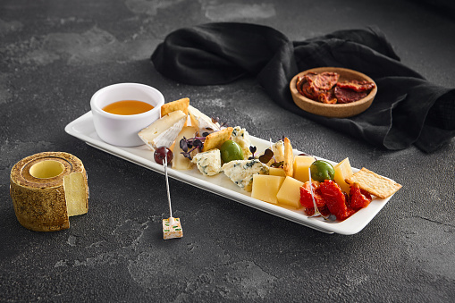 A curated selection of cheeses, sun-dried tomatoes, and olives, perfect for wine pairing, presented on a plate with minimalist style on a dark background.