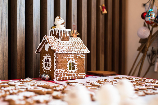 Christmas Gingerbread House with Window Lights in Winter Snowy Forest at Night. Creative Food Decoration Design for Xmas Holiday over Dark Background with Copy Space