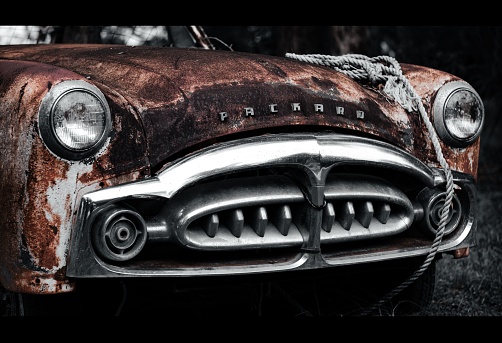 Kissimmee, United States – July 17, 2023: An abandoned vintage car, rusting in a dark, deserted area, its hood raised in a state of disrepair