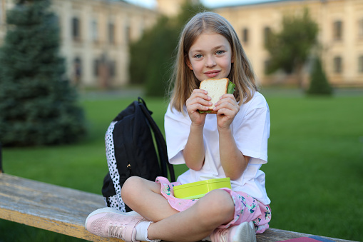 Young girl enjoying a healthy snack outdoors in the park, holding a sandwich with a joyful expression.