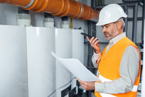 istock Handsome engineer with blueprints on industrial plant. Man with technical drawings in hands on oil and gas factory using phone for audio message 1807903486
