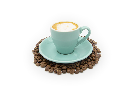 A macchiato cup and saucer on a white background surrounded by espresso beans