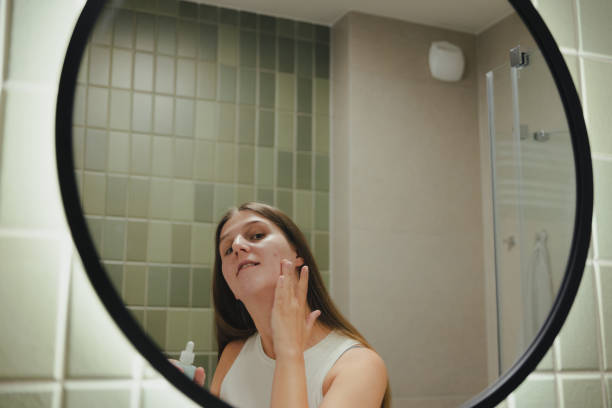 istock Smiling Woman Applying On Her Face Doing Acne Treatment in Bathroom 1807921686