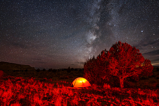 Camping Under the Stars in Canyon County USA - Tent lit up at night with stars and sky rotating with Earth's rotation. Night astrophotography time lapse.