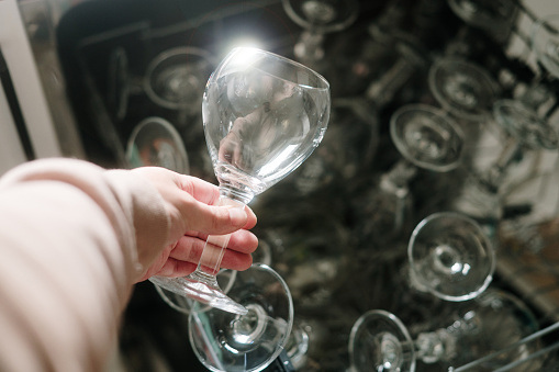 A hand holding a shiny glass cup by a dishwasher