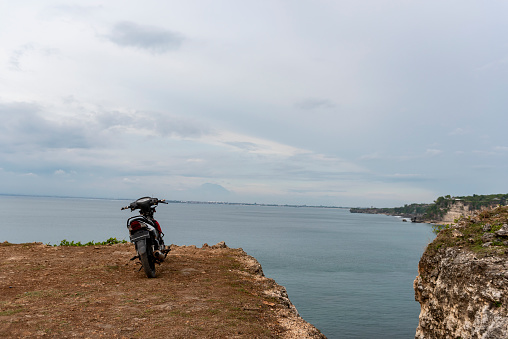 A small motorbike is parked on a cliff above the sea at Balangan Beach in Bali, Indonesia