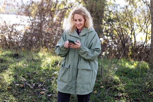 Mid adult woman using a mobile phone in nature. About 35 years old, Caucasian blonde.