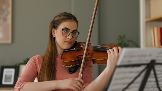 A teenage girl playing violin at home