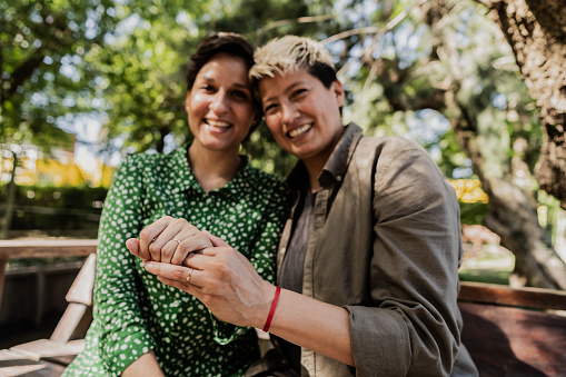 Portrait of a lesbian couple showing the engagement ring at natural parkland