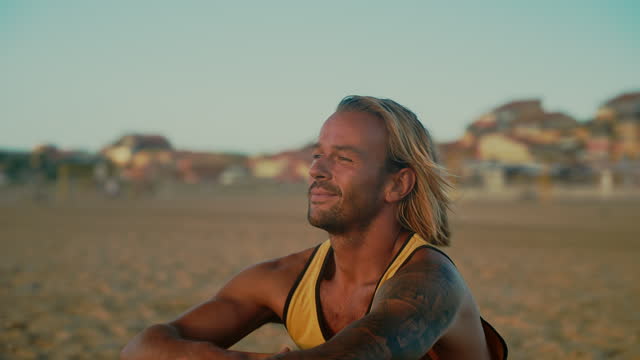 Smiling handsome blonde man with tattoos relaxing on sunny ocean beach