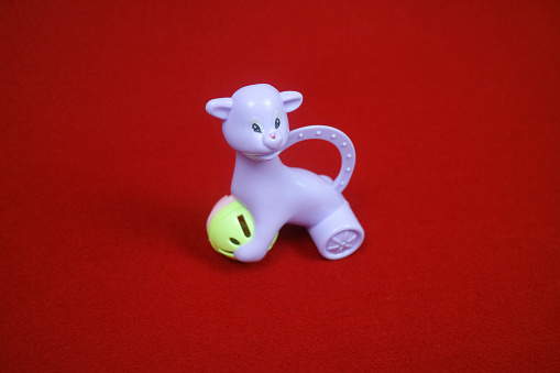 A toy shaped like an alpaca animal, purple in color, holding a ball. on a red background