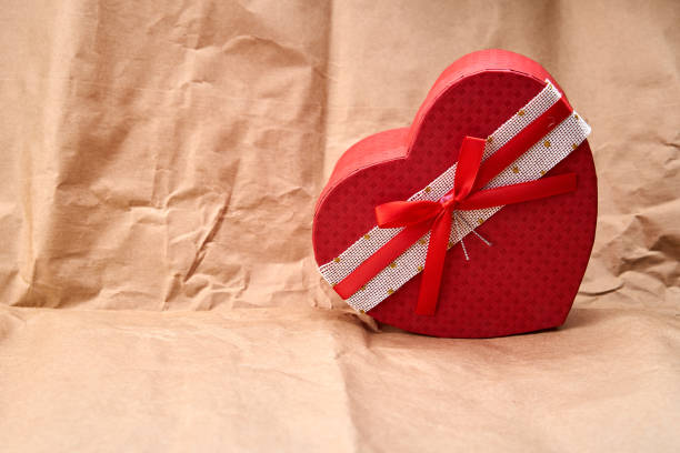 Red heart shaped gift on a cardboard textured background.