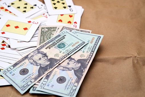 Poker cards and dollars lying on a cardboard-like surface.