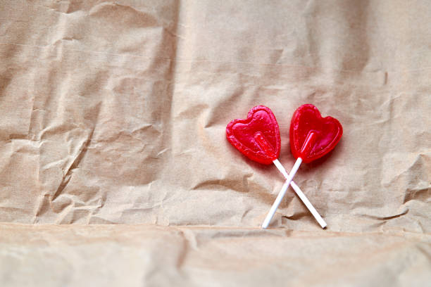 Two red heart-shaped lollipops together on a cardboard background.