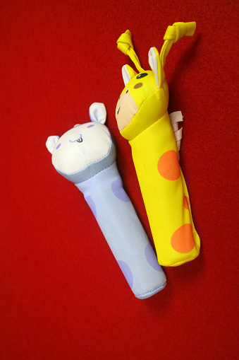 A yellow blue giraffe shaped baby holding toy that makes a sound when squeezed. on a red background