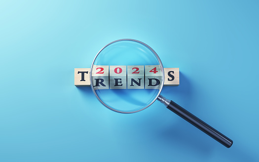 3d Render, 2024 Trends Written on Wooden Blocks Standing Selected with Magnifying Glass on Blue Background (close-up)