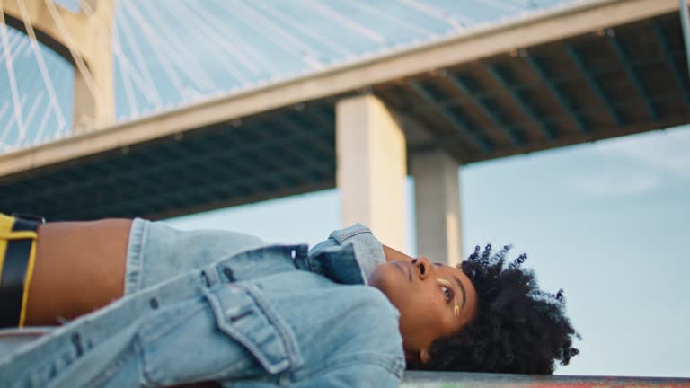 Black haired girl lying city street in front bridge close up. Woman posing town