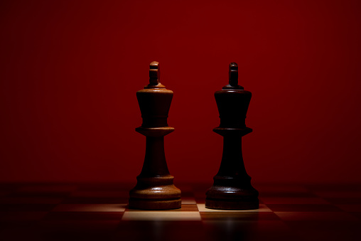 Two kings facing each other on a chessboard in a mysterious setting ready for battle on a red background