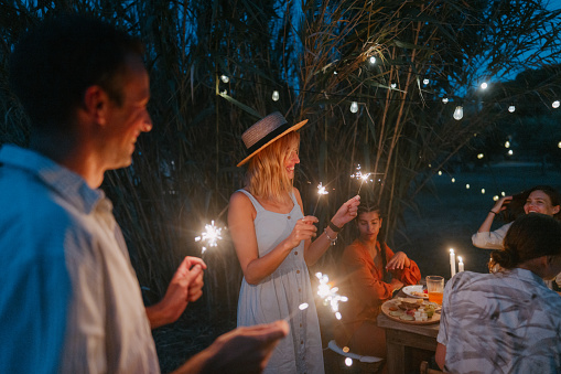 Photo of a loving couple attending an outdoors summer party, with a group of their friends