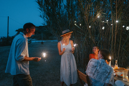 Photo of a loving couple attending an outdoors summer party, with a group of their friends