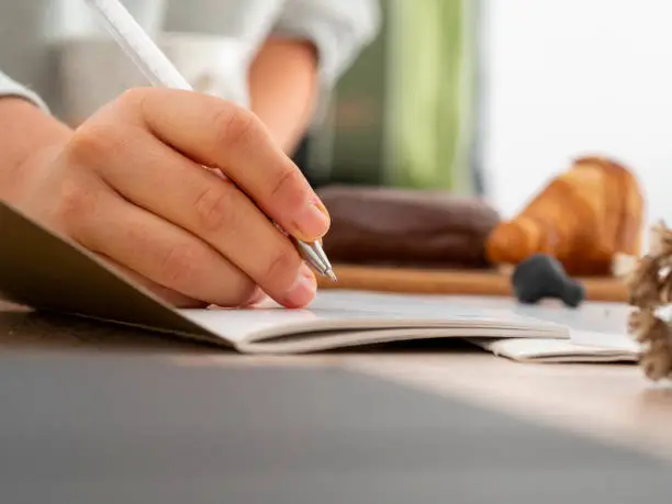 Close-up of a woman hand taking notes in a notebook with a ballpen during a working session on a desk. Productive meeting at work while taking minutes and planning.
