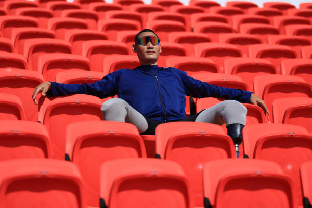 istock Asian man with a prosthetic running blade sitting on stadium bleachers 1808048009