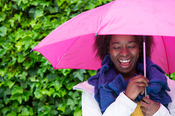 felice donna sotto la pioggia - candid women african descent umbrella foto e immagini stock