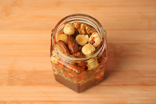 Different nuts and honey in jar on wooden table, above view