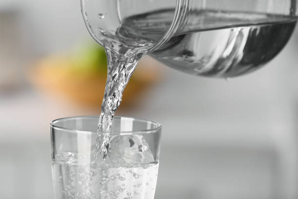 istock Pouring water from jug into glass on blurred background, closeup 1808053103