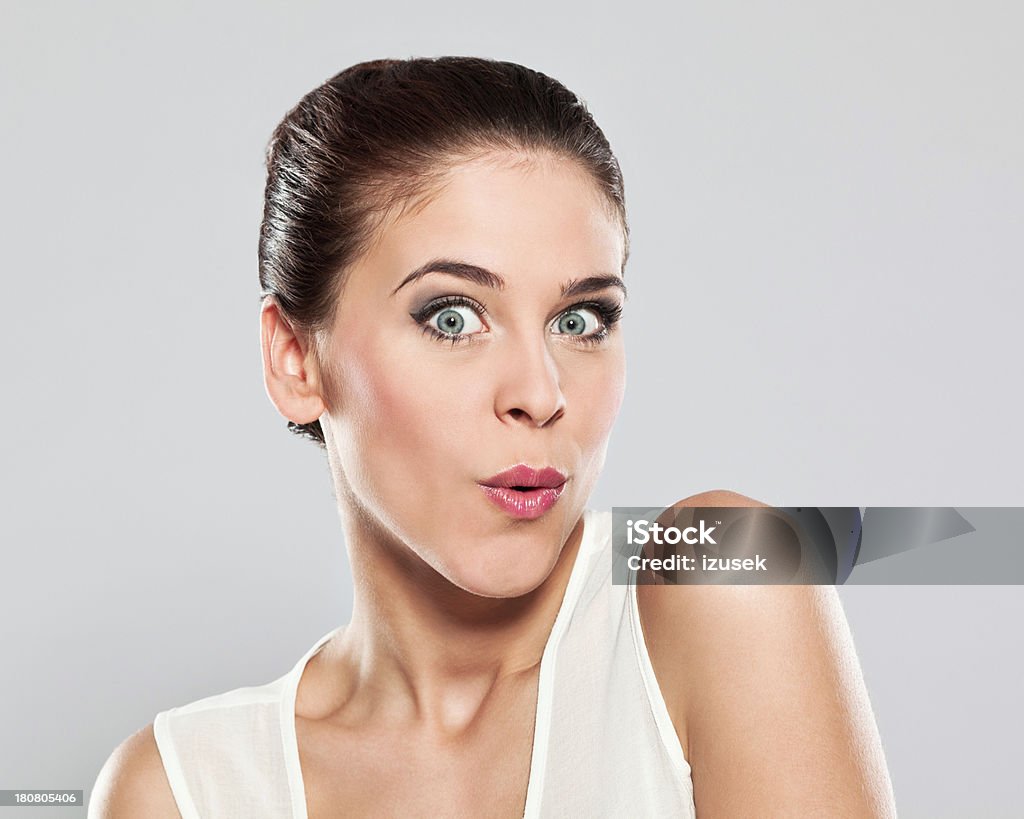 Attractive young woman, Studio Portrait Portrait of surprised young woman whistling at the camera. Studio shot on a grey background. 20-24 Years Stock Photo