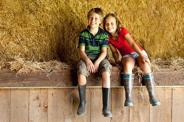 happy smiling children with gumboots sitting in old straw barn