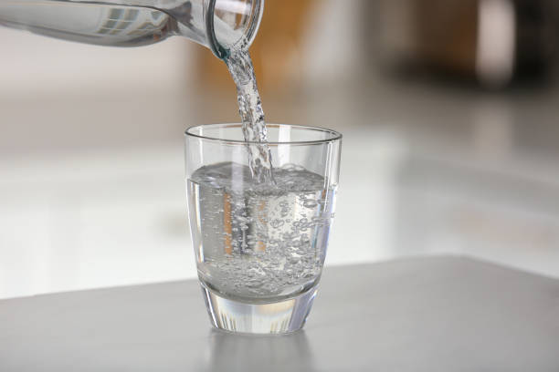 istock Pouring water from bottle into glass on light grey marble table in kitchen. Space for text 1808055962