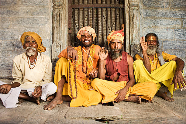 Sadhu - indian holymen sitting in the temple "In Hinduism, sadhu, or shadhu is a common term for a mystic, an ascetic, practitioner of yoga (yogi) and/or wandering monks. The sadhu is solely dedicated to achieving the fourth and final Hindu goal of life, moksha (liberation), through meditation and contemplation of Brahman. Sadhus often wear ochre-colored clothing, symbolizing renunciation." caste system stock pictures, royalty-free photos & images