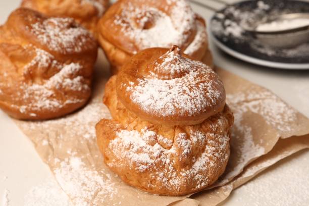 istock Delicious profiteroles with powdered sugar on parchment paper, closeup 1808063176