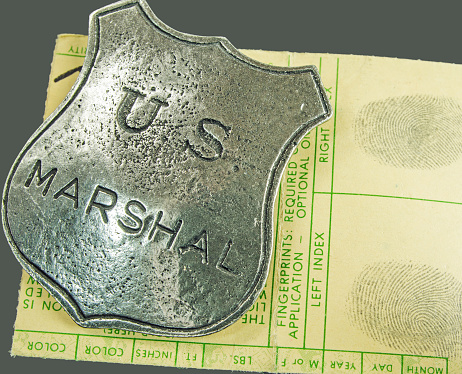 An antique marshal on a set of fingerprints and law enforcement document. Black background.